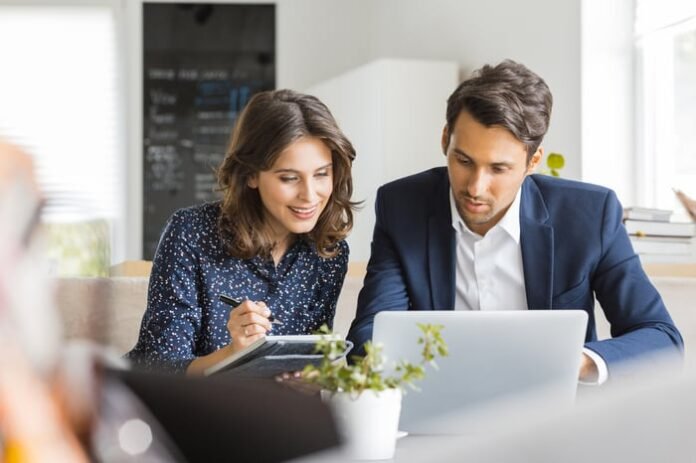 Two investors in an office are studying something on a laptop.