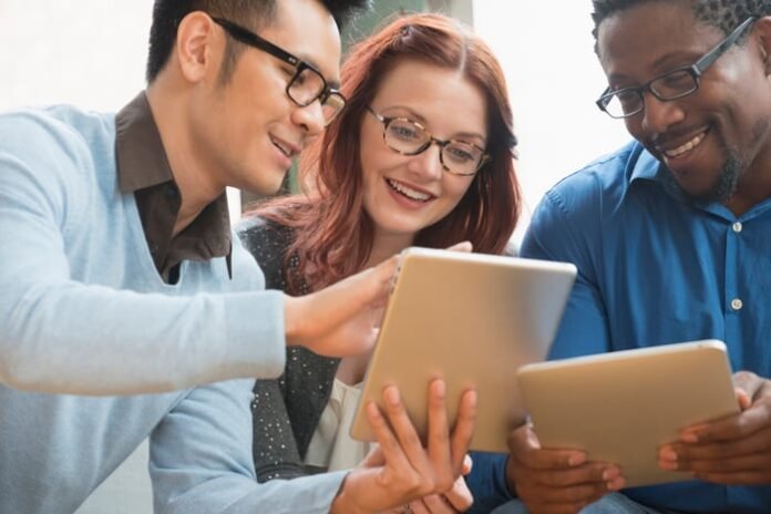 Three investors smile as they gather around a tablet.