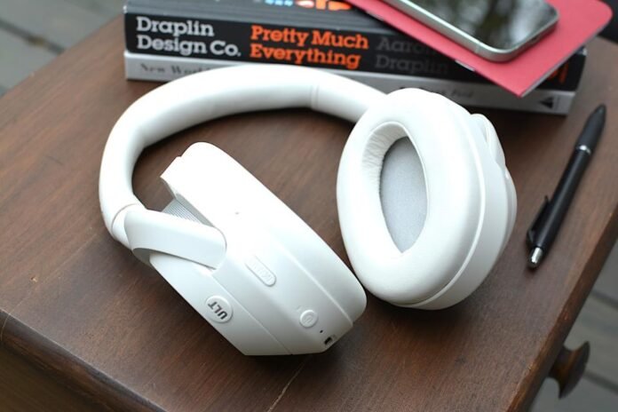 White headphones sitting on a wooden table from above with a red notebook and phone in the background, on top of a black and white book.