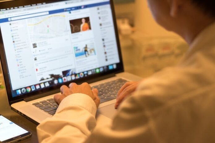 Person sitting at a table and using Facebook on a laptop.